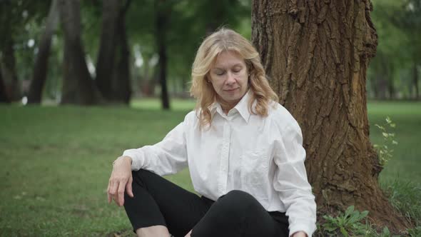 Side Angle View of Confident Caucasian Businesswoman Taking Off Eyeglasses and Sitting in Yoga Pose