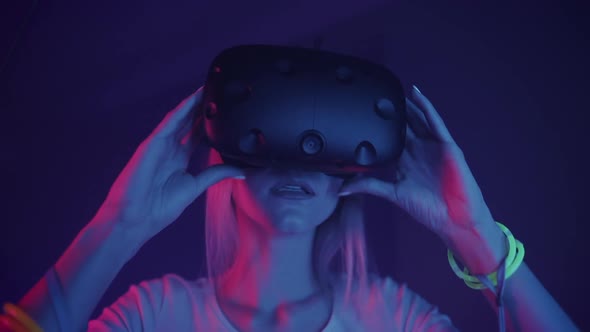 Portrait of Young Beautiful Woman Removing Virtual Reality Headset on the Cyber Lighting Background.