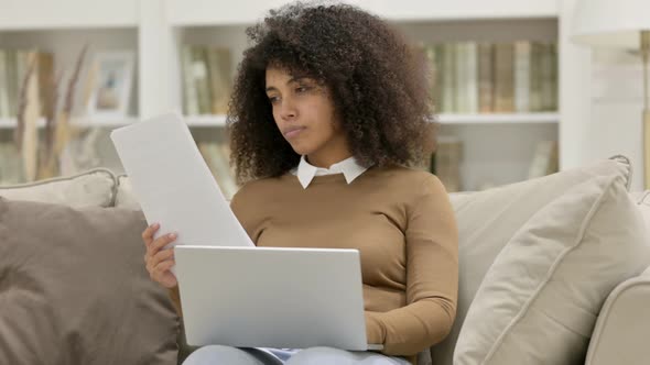 Young African Woman with Documents Working on Laptop on Sofa