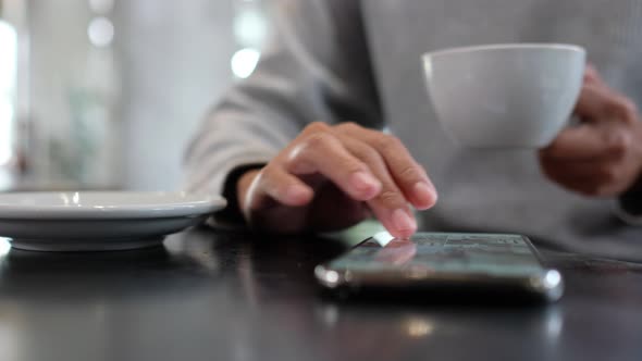 Closeup of a woman touching and scrolling on smart phone screen while drinking coffee