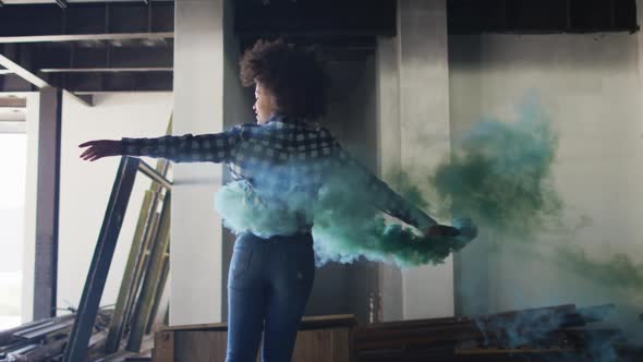 Mixed race woman holding green flare dancing in an empty building