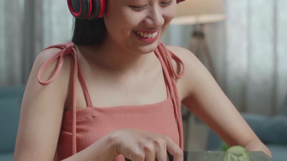 Close Up Of Asian Woman Enjoys Listening To Music With Headphones While Slicing The Cucumber At Home