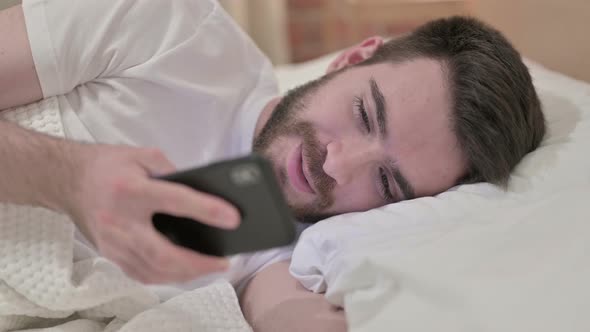 Handsome Young Man Using Smartphone in Bed 
