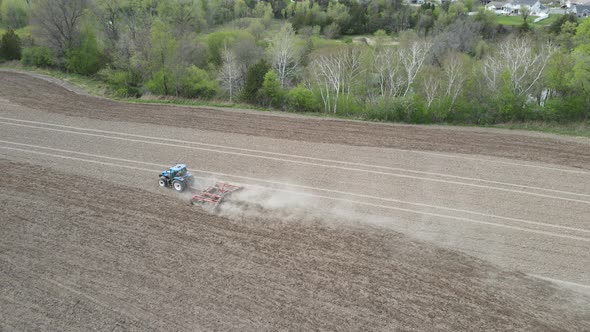 Overhead view of farmer discing field in preparation for planting in the midwest. Trees line creek.