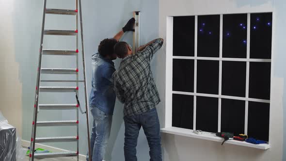 Black Constructors Check Wall with Level Working in Studio