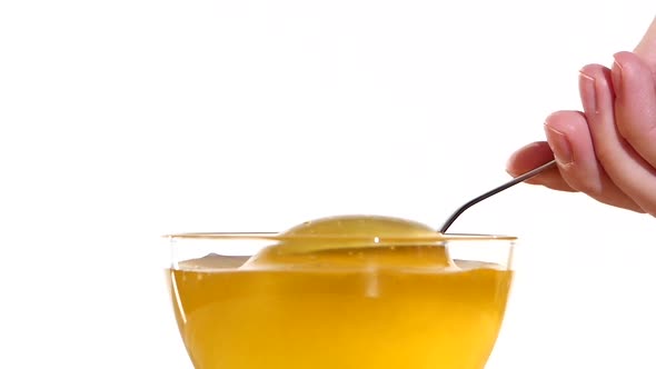 Hand Taking Honey From Glass Bowl Using Metal Spoon, on White, Slow Motion