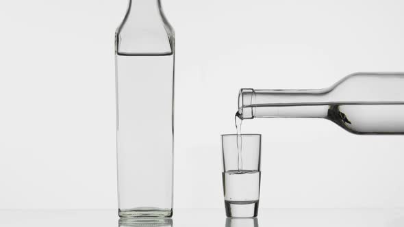 Pouring Up Shot of Vodka From a Bottle Into Glass. White Background