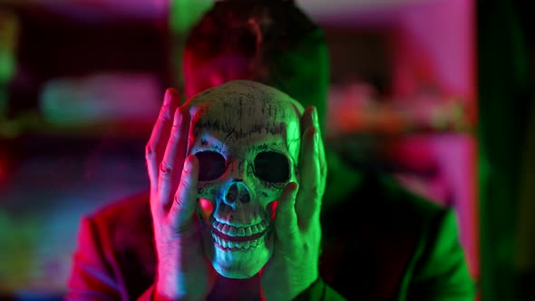 a Man Out of Focus and Wearing a Black Knitted Mask Without Eyes Holds a Skull in Front of Him in a