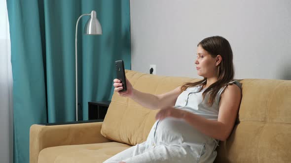 Young Pregnant Woman Taking Pictures of Herself on the Phone While Sitting on the Couch