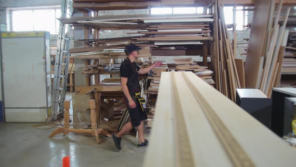 Carpentry Workshop  a Man Worker Walks Along the Shelves and Takes a Triangle Board