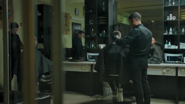 Two Clients and Two Hairdressers Haircut in a Dark Barbershop Room