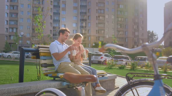 Happy Young Couple Resting After Cycling on a Bench on a Sunny Summer Day