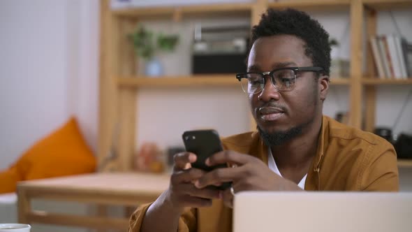 African American Man Use Smartphone Device and Type Text Message Sitting at Home Office