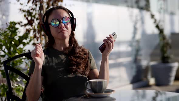 Portrait of a Happy Adult Woman in a Street Cafe Listening to Music Through Headphones with Stylish