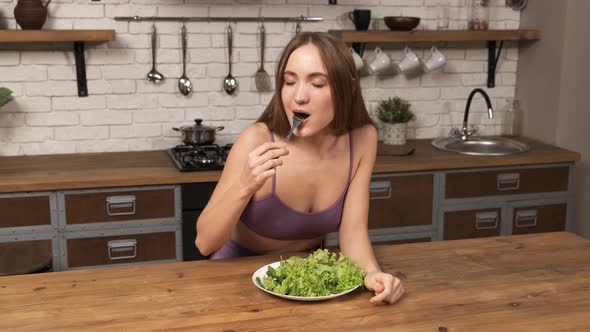 Young Fitness Female in a Sportswear Eats a Salad with Pleasure in the Home Kitchen