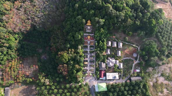 aerial drone of a unique temple with a golden buddha on a mountain surrounded by coconut trees in Ao