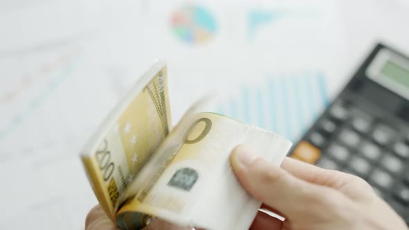 A Businessman Hands are Counting Euro Bill Notes on Background of Calculator and Graphs