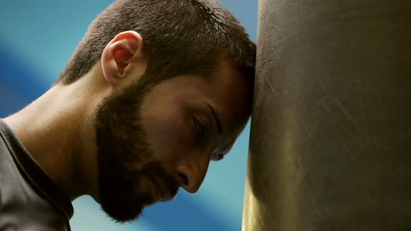 Young Sweaty Boxer is Resting on Punching Bag