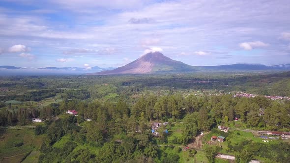 Reverse drone shot of Mount Sinabung volcano and the surrounding beautiful green village in Berastag