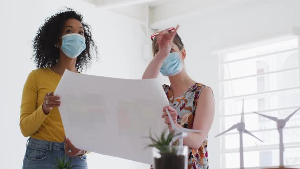 Two woman wearing face mask discussing over document at office