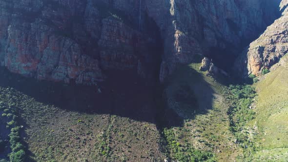 Aerial - Tilt-up shot towards rugged sandstone mountains with waterfall