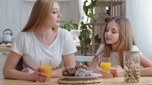 Mother and Daughter Teenager Child Girl Sitting Together at Table in Kitchen Drinking Natural Orange