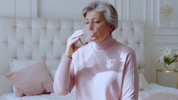 Aged Woman Holding Glass Feeling Thirsty or Dehydrated, Drinking Fresh Pure Aqua Following Healthy