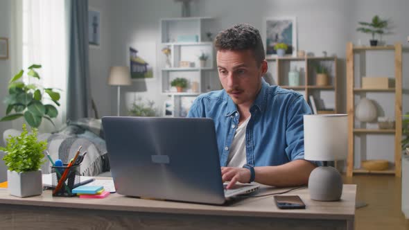 A Young Man in the Living Room Starts Working on a Laptop