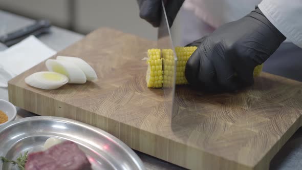 Hands of a Professional Unrecognized Chef in Black Gloves Are Chopping Corn Into Round