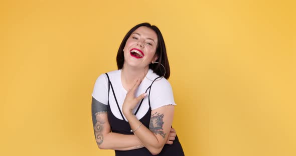 A young embarrassed woman with tattoo is listening compliments shy and laughing in yellow studio
