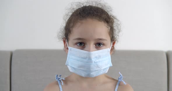 Portrait Cute Small Child or Little Girl in a Protective Medical Mask with a Sad Disappointed Face