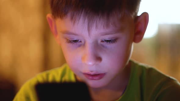 Caucasian preschooler carefully looks at the smartphone screen.