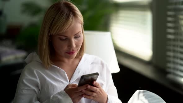 Blonde Woman Is Using Smartphone, Typing Message at Social Nets, Wifi at Home