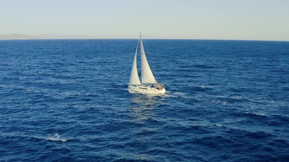 Sailing boat with white sails, cloudy sky and rippled sea background