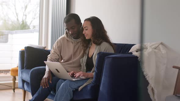 Relaxed Young Couple At Home Sitting On Sofa Browsing Internet On Laptop Computer