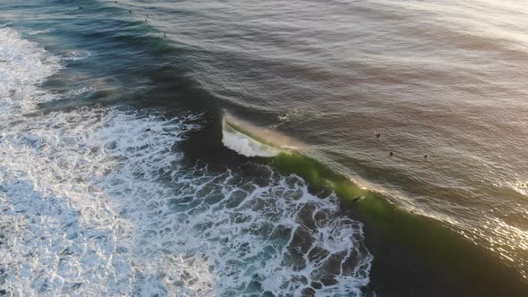 A drone rotates around an aerial view of surfers surfing and waves crashing.