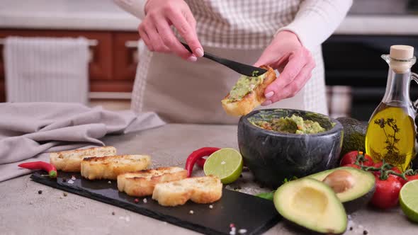 Woman Making Bruschetta with Freshly Made Guacamole Sauce at Domestic Kitchen