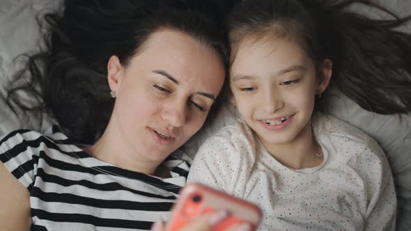 A Mother and a Teenage Daughter Lie Together on the Bed and Watch Photos or Videos on a Smartphone