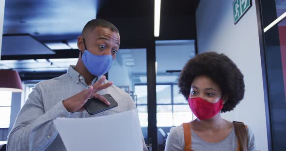 Diverse business people wearing face masks walking and using digital tablet in modern office