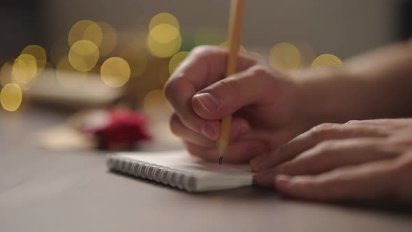 Slow Motion Orbit Shot Man Writes Christmas Gifts Notepad Pencil Under Warm Light Evening