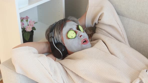 Woman with facial mask and cucumbers on face listening to music