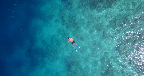 Young man snorkel over clear sea water near shore of tropical island, watching fish swim through cor
