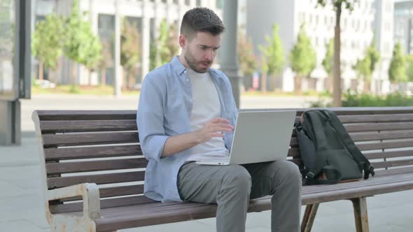 Young Man Reacting to Loss on Laptop While Sitting on Bench