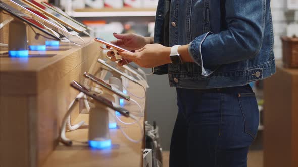 Unrecognizable Woman Chooses a Smartphone in an Electronics Store.