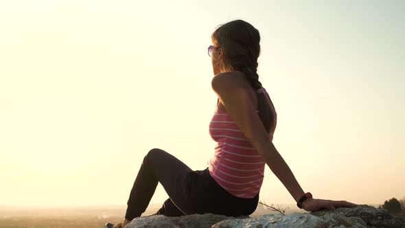 Young relaxed woman sitting outdoors on a big stone enjoying warm summer day. Girl meditating