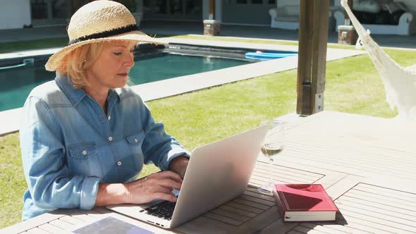 Senior woman using laptop near swimming pool