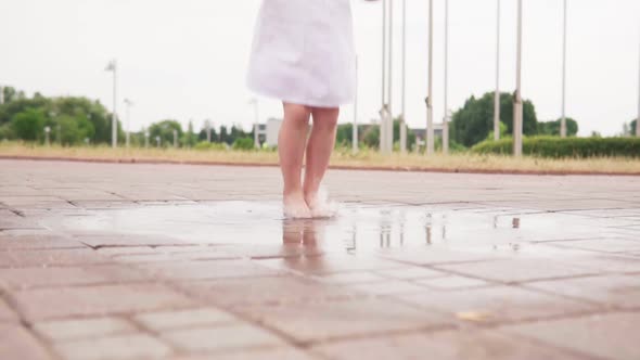 Child Barefoot Jumps in Puddle on City Street