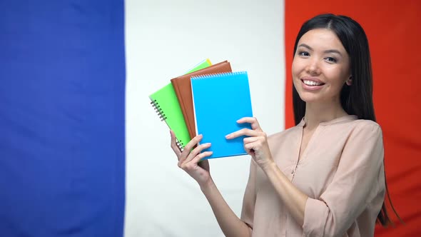 Smiling Asian Lady Showing Copybooks Against French Flag Background, Lessons