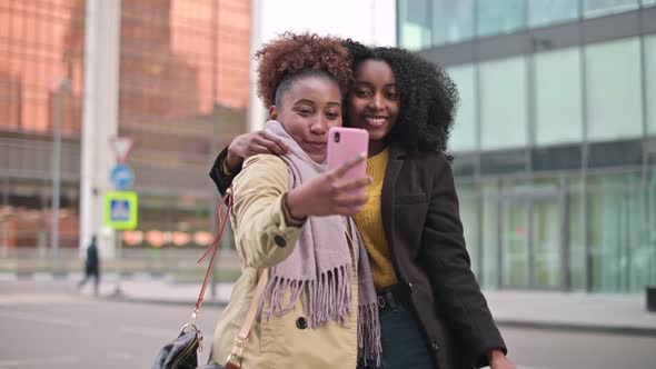 Two smiling young women take a selfie on the background of city landscapes