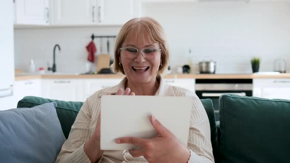 Woman At Home On Couch Communicates Via Video On Tablet With Family And Friends